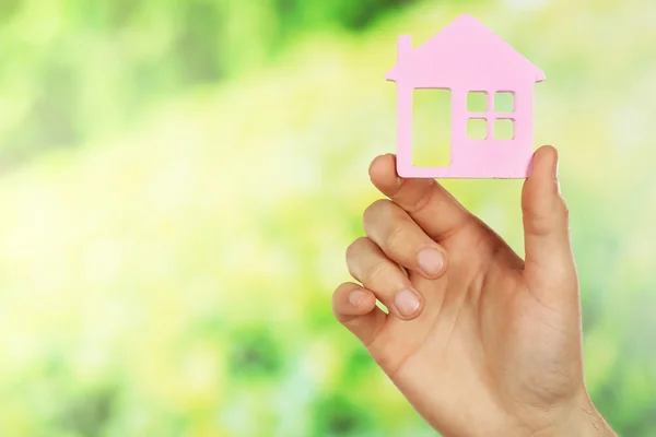 Feminino mão segurando casa no verde desfocado fundo — Fotografia de Stock