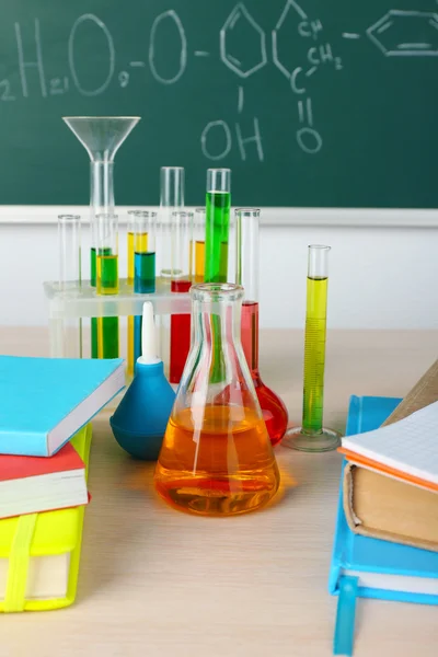 Stůl v chemické učebně s zkumavky na pozadí zelených tabule — Stock fotografie