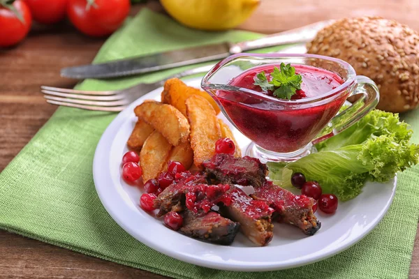 Beef with cranberry sauce, roasted potato slices on plate, on wooden background — Stock Photo, Image