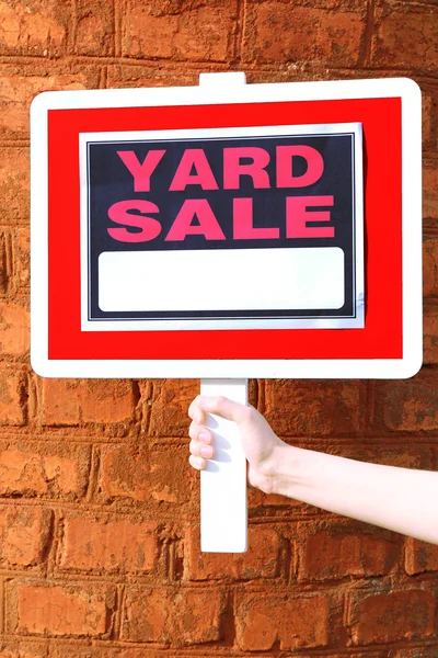Ξύλινη πινακίδα πώλησης ναυπηγείων στο θηλυκό χέρι σε φόντο κόκκινο τούβλο τοίχων — Φωτογραφία Αρχείου