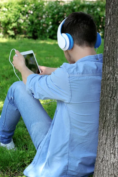 Hombre con auriculares descansando bajo el árbol en el parque —  Fotos de Stock