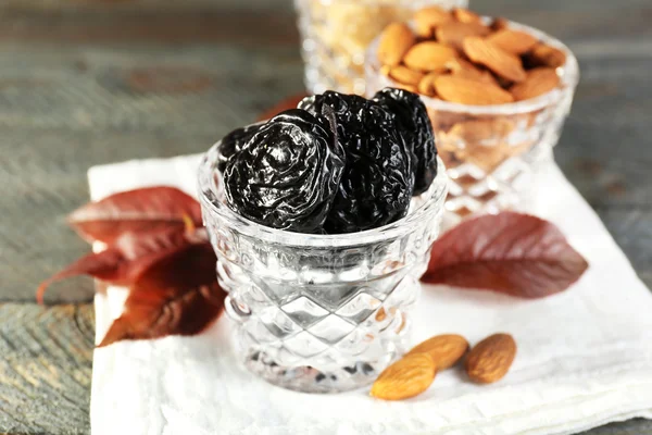 Pruneaux et amandes dans des verres à feuilles de raisin sur table en bois, gros plan — Photo