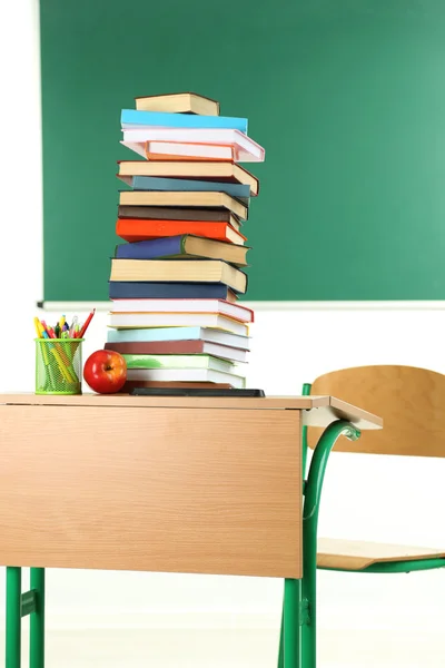 Wooden desk with books and chair in class on blackboard background