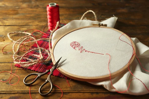 Il cerchio da ricamo con tela e fili da cucito rossi sul tavolo da vicino — Foto Stock