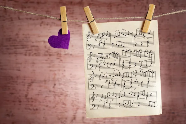 Světlé srdce a hudební list visí na laně na dřevěné pozadí — Stock fotografie