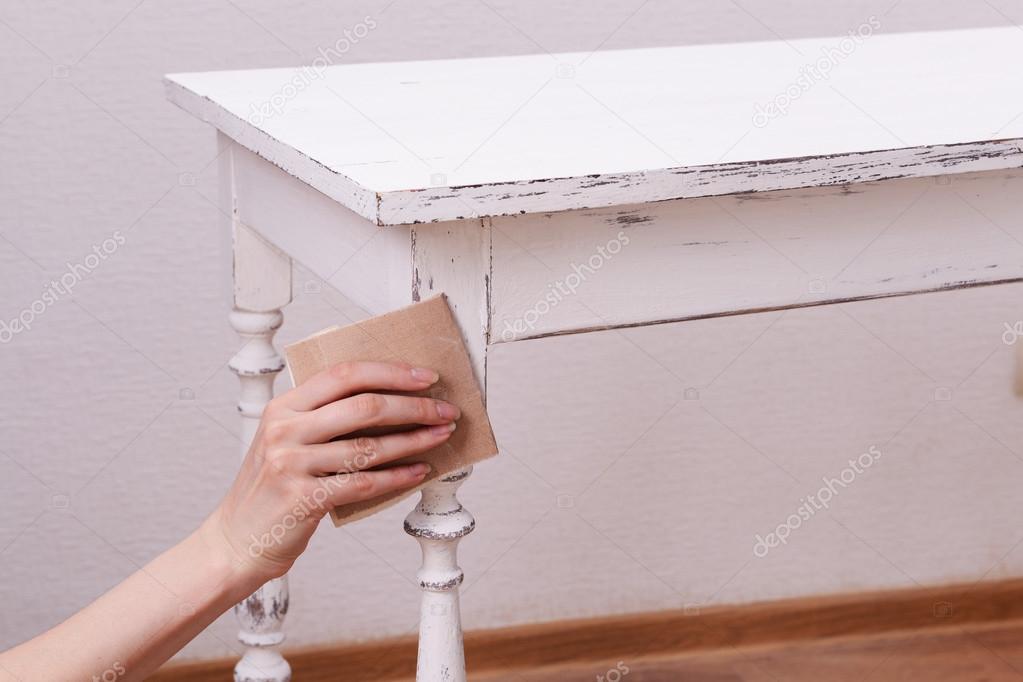 Female hand removing paint from wooden table for decoration, indoors