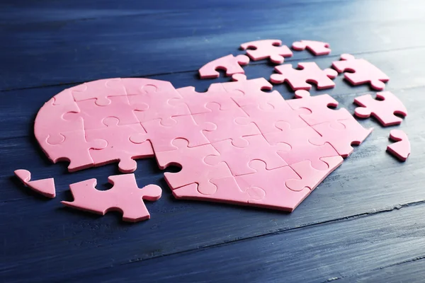 Corazón rompecabezas rosa sobre fondo de madera — Foto de Stock