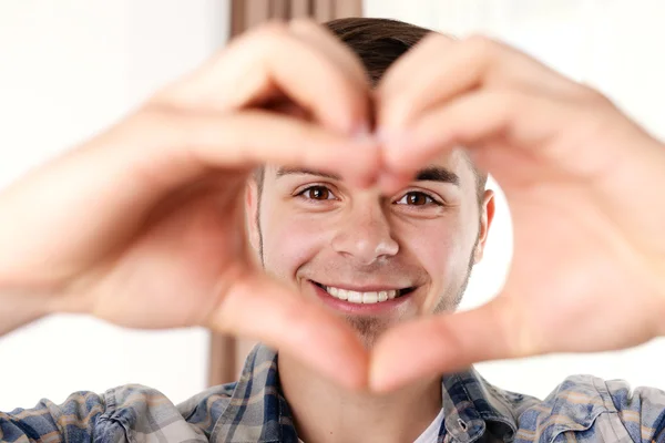 Çekici bir genç adam gülümseyen parmaklarını kullanarak kalp sağlar — Stok fotoğraf