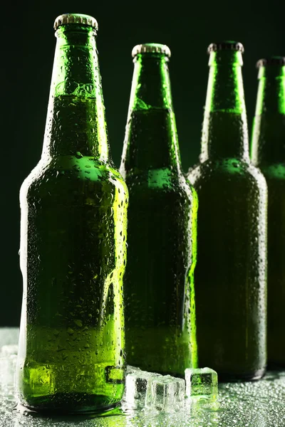 Garrafas de vidro de cerveja com cubos de gelo no fundo escuro — Fotografia de Stock