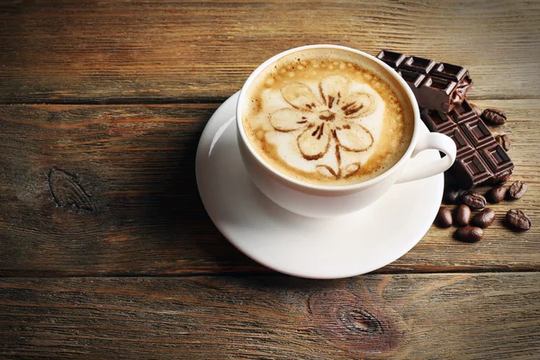 Tasse de café latte art avec des grains et du chocolat sur fond en bois — Photo