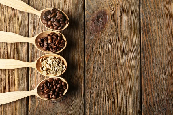 Kaffeebohnen in Löffeln auf Holzgrund — Stockfoto