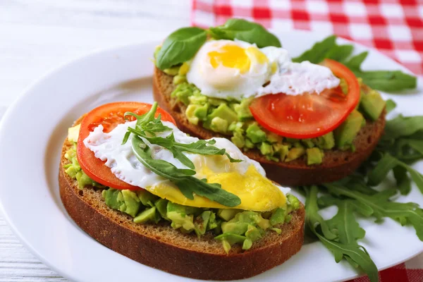 Sabrosos sándwiches con huevo, aguacate y verduras en plato, sobre fondo de madera — Foto de Stock