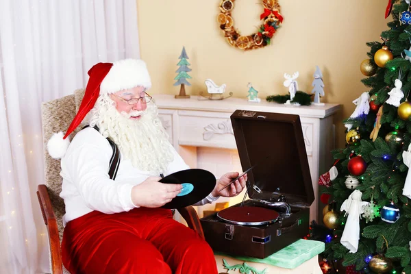 Santa claus zittend in een comfortabele stoel in de buurt van retro draaitafel thuis — Stockfoto