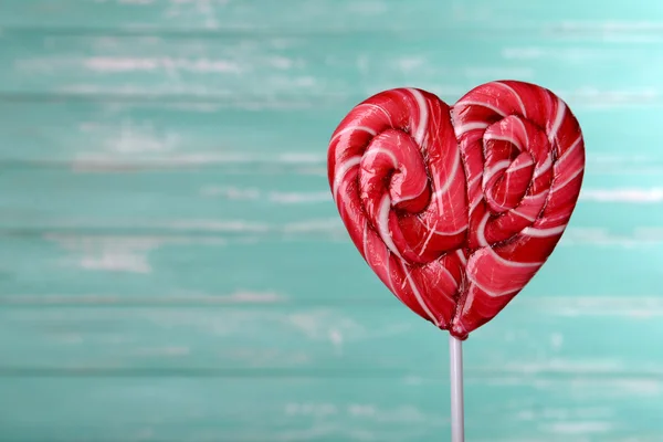 Bright lollipop in shape of heart on wooden background