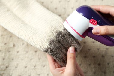 Female hands with Wool shaver on wool sweater background clipart