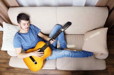 Odadaki kanepede gitarlı genç adam.