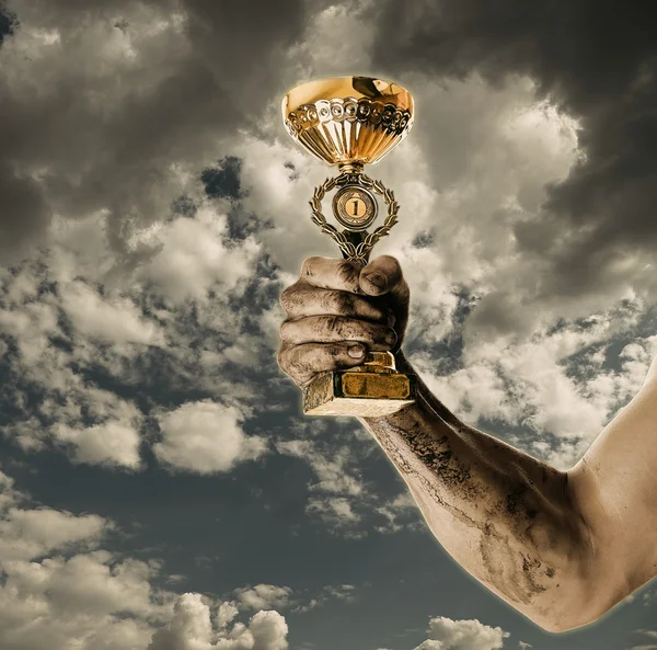 Gold cup in dirty hands on sky background — Stock Photo, Image