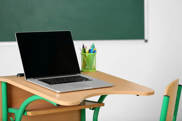 Scrivania in legno con cancelleria e laptop in classe su sfondo lavagna — Foto Stock