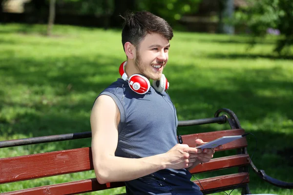 Uomo con cuffie poggiate su panchina nel parco — Foto Stock