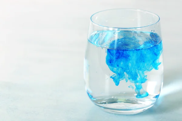 Vidro de água com tinta azul na mesa de perto — Fotografia de Stock