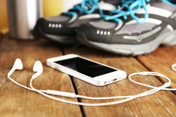 Sneakers and earphones on wooden table, closeup — Stock Photo, Image