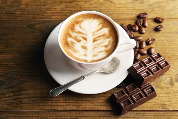 Tasse de café latte art avec des grains et du chocolat sur fond en bois — Photo