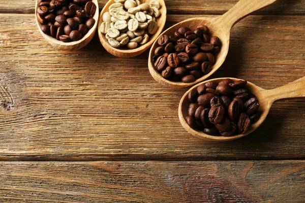 Kávová zrna v lžíce na dřevěné pozadí — Stock fotografie