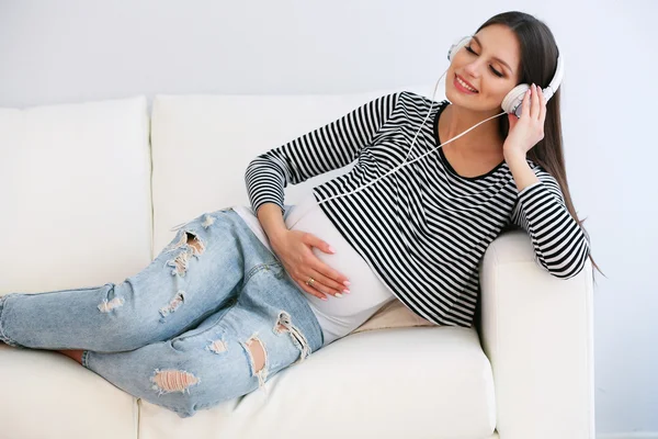 Pregnant woman with headphones on sofa in room — Stock Photo, Image