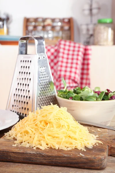 Grated cheese on wooden table in kitchen, closeup — Stock Photo, Image