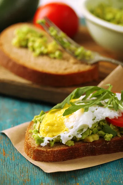 Sabroso sándwich con huevo, aguacate y verduras en servilleta de papel, sobre fondo de madera de color — Foto de Stock