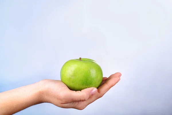 Weibliche Hand mit Apfel auf buntem Hintergrund — Stockfoto