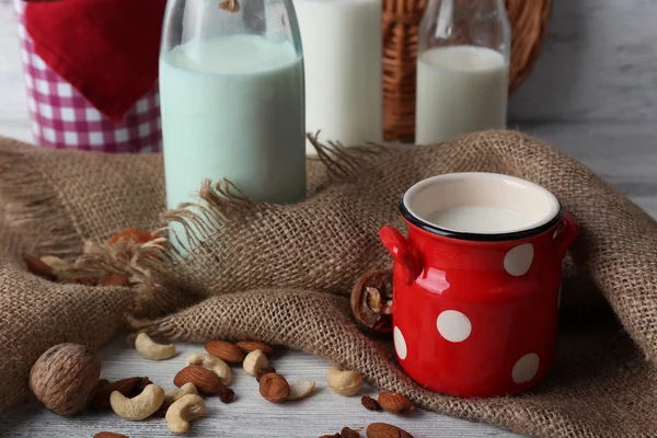 Latte in bicchieri e noci su tavola di legno con sacco, primo piano — Foto Stock