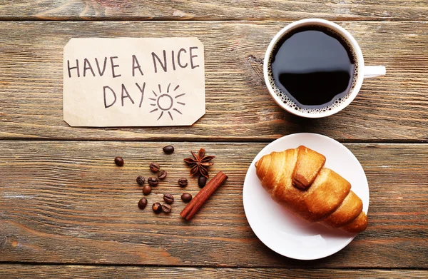 Tasse Kaffee mit frischem Croissant und eine schöne Tagemassage auf Holztisch, Blick von oben — Stockfoto