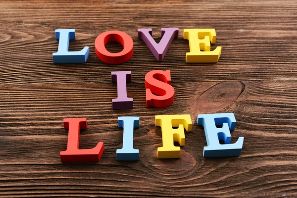 Надпись LOVE IS LIFE made of colorful letters on wooden background — стоковое фото