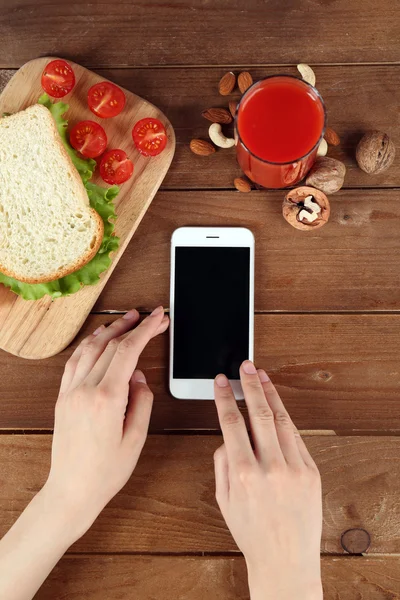 Еда и мобильный телефон в женских руках на деревянном фоне — стоковое фото