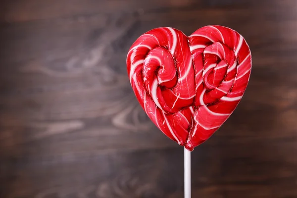 Bright lollipop in shape of heart on wooden background