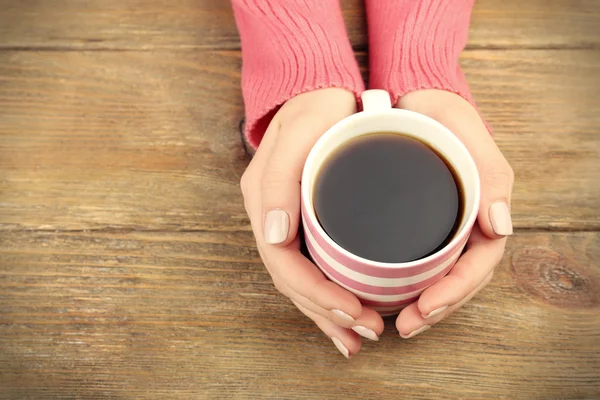 Kvinnliga händer som håller kopp kaffe på trä bakgrund — Stockfoto