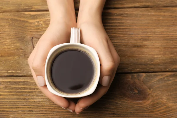 Manos femeninas sosteniendo taza de café sobre fondo de madera —  Fotos de Stock