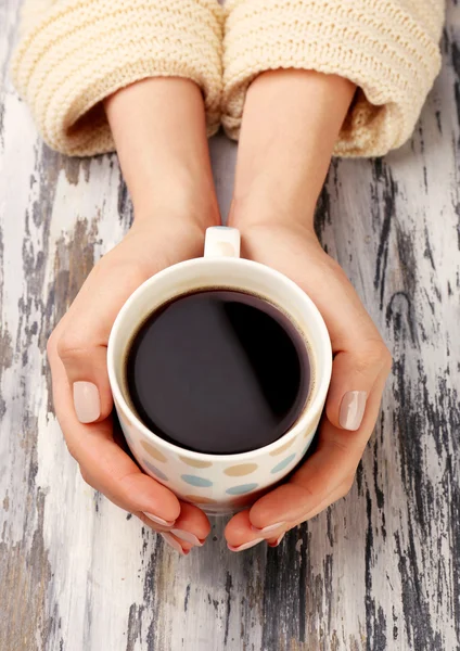 Mãos femininas segurando xícara de café no fundo de madeira — Fotografia de Stock