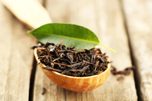 Black tea with leaf in spoon on old wooden table — Stock Photo, Image