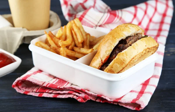 Tasty burger and french fries on plate, on wooden table background. Unhealthy food concept — Stock Photo, Image