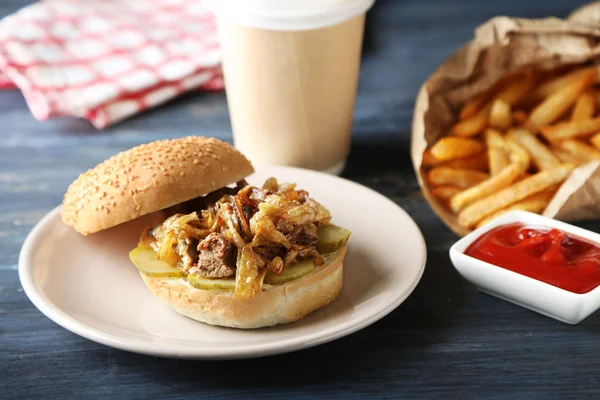 Sabrosa hamburguesa y papas fritas en plato, sobre fondo de mesa de madera. Concepto de alimentos poco saludables —  Fotos de Stock