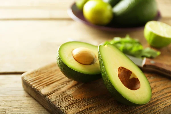 Avocado affettato e lime limone sul tagliere, su fondo di legno — Foto Stock