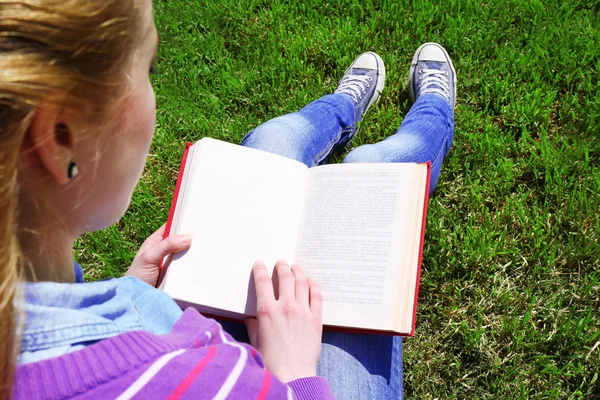 Молода жінка з книгою сидить на зеленій траві на відкритому повітрі — стокове фото