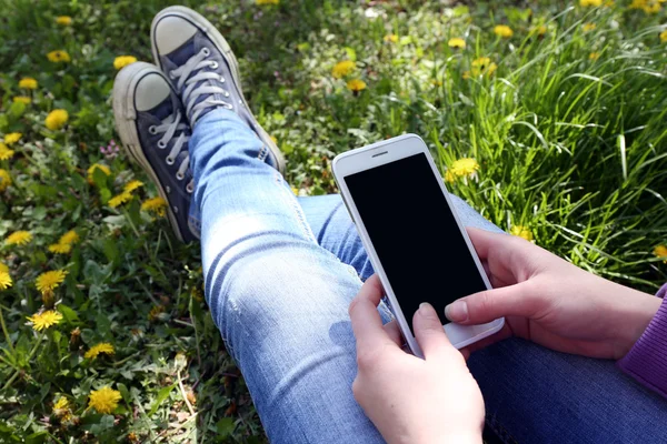 Ung kvinna med mobiltelefon sitter på grönt gräs utomhus — Stockfoto