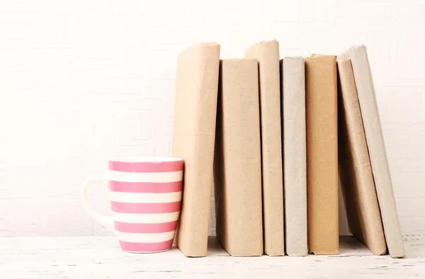 Books and cup on wooden shelf on wallpaper background — Stock Photo, Image