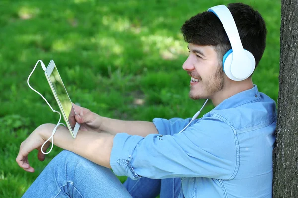 Homem com fones de ouvido descansando debaixo da árvore — Fotografia de Stock