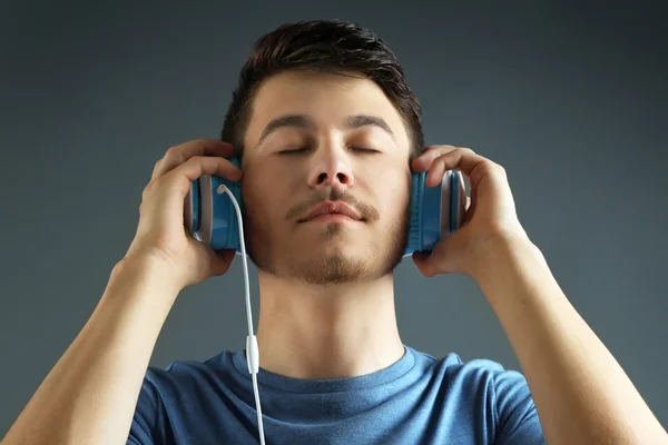 Bonito jovem ouvindo música em fundo cinza — Fotografia de Stock