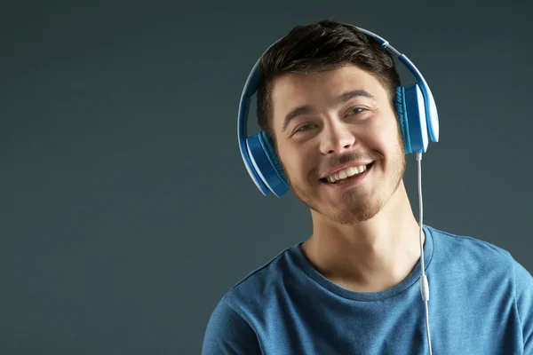 Handsome young man listening to music on grey background — Stock Photo, Image