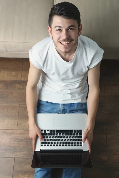 Jonge man zittend op de vloer met laptop in de kamer — Stockfoto